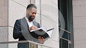 Serious African American ethnic businessman entrepreneur man employer company CEO standing on balcony in office holding