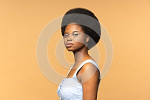 Serious African American female with afro hairstyle look at camera,  beige studio background