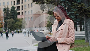 Serious african american girl blogger using laptop, sitting outdoor, young busy focused businesswoman looking at screen