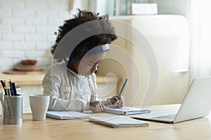 Serious African American little girl wearing headphones writing notes