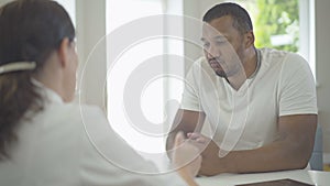 Serious African American man shaking hands with Caucasian woman in hospital. Portrait of patient on medical consultation