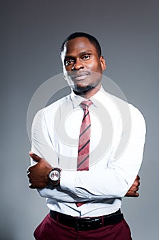 Serious african american man in shirt and tie folds his arms over his chest and stands against gray background