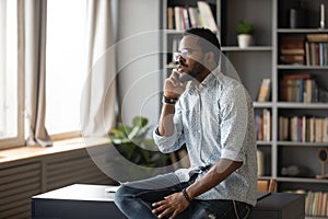 Serious African American man talking on phone, sitting on desk photo