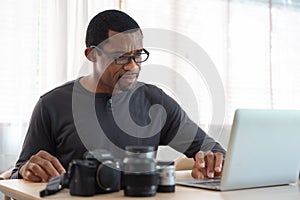 Serious African American photographer man using laptop computer