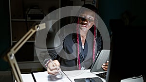 Serious african american woman boss takes business notes on touchpad, focused in the office night light, with dark glasses on,