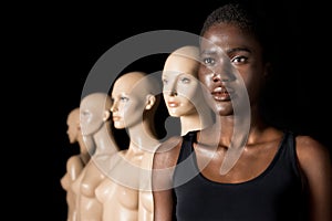 serious african american woman in swimsuit standing in row with mannequins