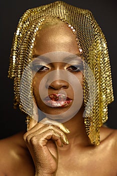 Serious african or black american woman wearing golden headdress and bright make-up placing finger on her chin