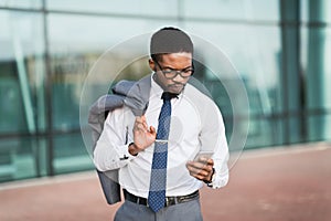 Serious African Businessman Texting Standing With Travel Suticase Near Airport