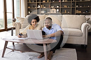 Serious African couple paying bills online, calculate expenses at home