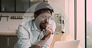 Serious african man do telecommute job using laptop in kitchen