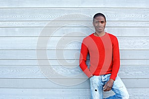 Serious african man with red sweater leaning against wall