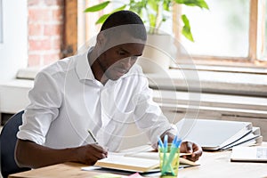 Serious african man university student studying reading textbook making notes