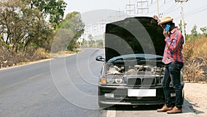 Serious african man using smart phone side the broken car