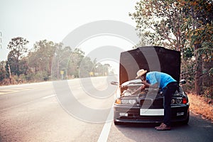 Serious african man using smartphone and holding his head by hands standing near his old broken car  with raised hood on the