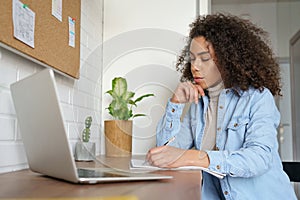 Serious african teen girl college student elearning at home making notes.