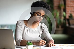 Serious african woman studying using internet holding pen writing notes photo