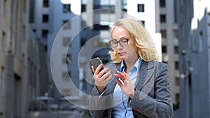 Serious aged lady boss checking meeting schedule app by smartphone, internet