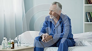 Serious aged man sitting upset and pensive on bed at home, lonely sick person photo