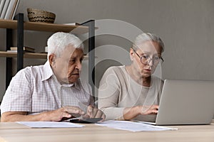 Serious aged spouses sit at desk manage household finances