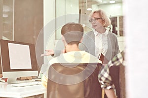 Serious aged woman, female company executive training new employee, monitoring progress and criticising his work while