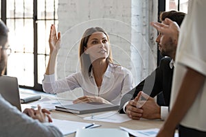 Serious ambitious businesswoman raise hand ask question to diverse presenter.