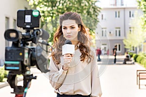 serious anchorwoman with microphone standing in front of digital