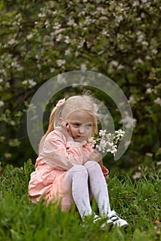 Serious or angry little girl sitting on the ground with flowers in her hands. Childrens resentment. Vertical frame