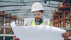 Serious Arab guy engineer checking construction plan and looking around outdoors