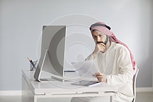 Serious Arab man thinks sitting at a table with a computer analyzes looking at paper.