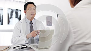 Serious Asia male doctor in white medical uniform using computer laptop is delivering great news talk discuss results or symptoms