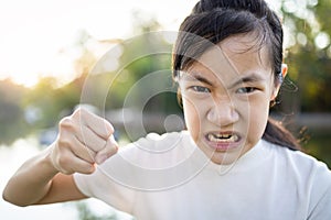 Serious asian child girl with her fist raised for threat warning or quarreling,angry female threatening with fist,about to punch, photo