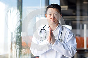 Serious asian doctor looking at webcam listening to patient interlocutor online, man working remotely from clinic