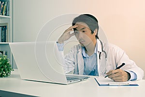 Serious Asian Doctor and Stethoscope Write Report and Using Laptop Computer in Vintage Tone