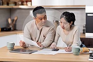 Serious asian family counting monthly expenses, kitchen interior