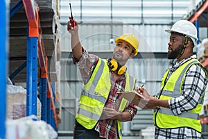 Serious Asian foreman holding walkie talkie and African engineer in safety hat look at inventory, working at site, listing problem