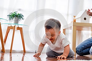 Serious Asian little boy crawling on floor while young father sitting next to him in living room