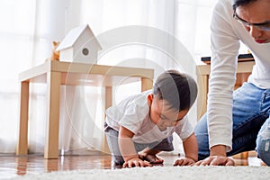 Serious Asian little boy crawling on floor while young father sitting next to him in living room