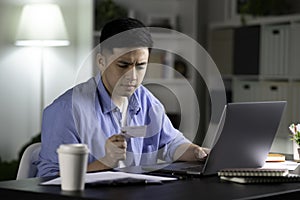 Serious Asian man doing online shopping, making online payment transaction using laptop  at home