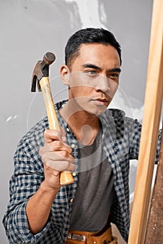 A serious Asian man uses hammer to hit wood while doing home renovation DIY