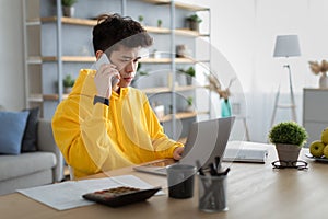 Serious asian man working and talking on phone at home