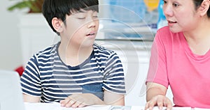 Serious Asian mother with son doing homework in the living room.