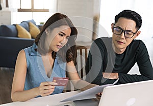 Serious Asian wife checking analyzing statement utilities bills sitting together at home