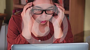 Serious Asian woman feeling headache after working on computer laptop for a long time indoors. Health and Office syndrome concept.