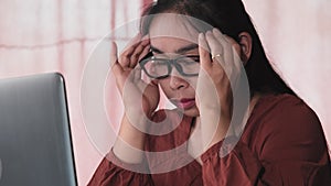 Serious Asian woman feeling headache after working on computer laptop for a long time indoors. Health and Office syndrome concept.