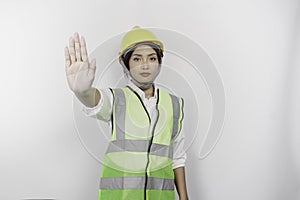 Serious Asian woman labor wearing safety helmet and vest with hand gesture pose rejection or prohibition, isolated by white