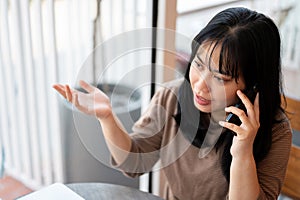 A serious Asian woman is talking on the phone with someone while sitting in a cafe