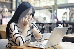 Serious asian woman thinking of problem to working a difficult assignment in a desktop, using laptop computer sitting alone at