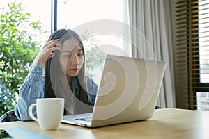 Serious Asian woman using a laptop working at home.
