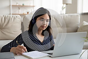Serious Asian woman wearing headphones looking at laptop screen