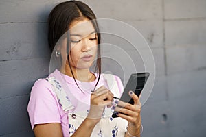 Serious Asian young woman using her smartphone with a pen or stylus,outdoors.